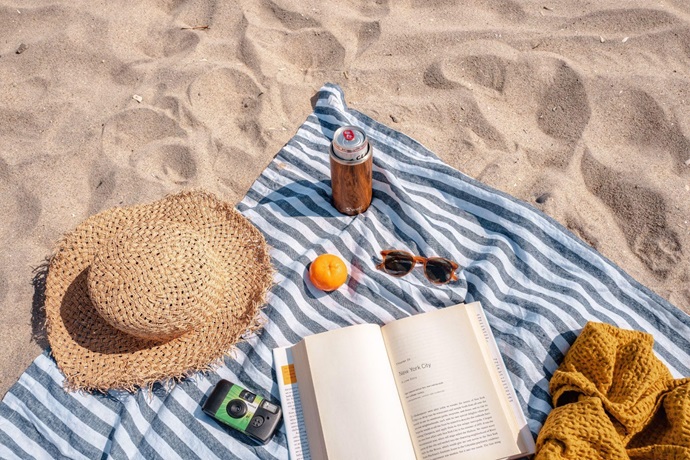 A hat, camera, and book on a blanket at a beach that you can travel to with Royal Holiday Vacation Club